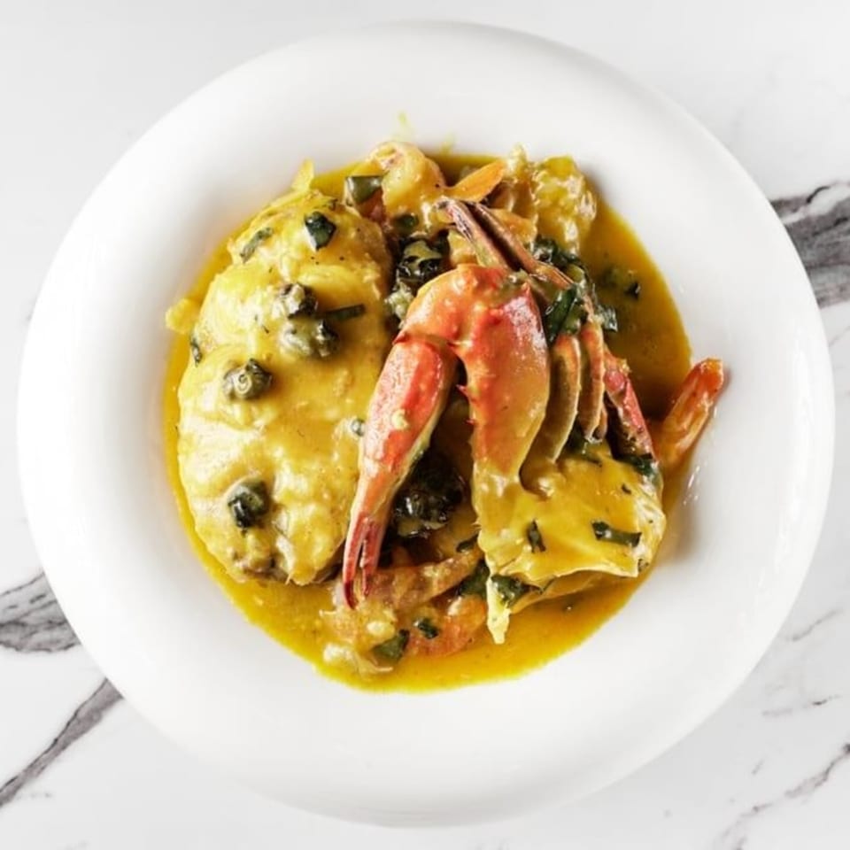 African-style crab and seafood stew in a rich yellow sauce with greens, served in a white bowl.