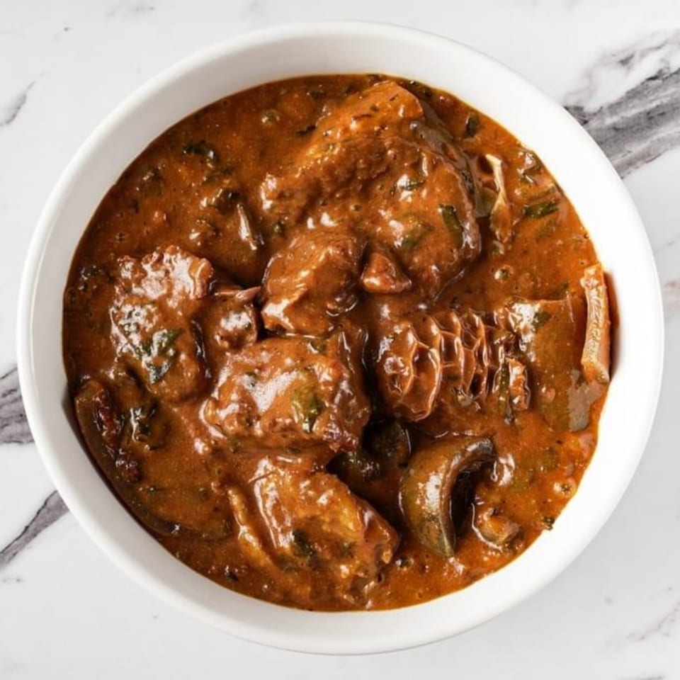 A bowl of rich, reddish-brown African stew with meat and vegetables on a marble surface.