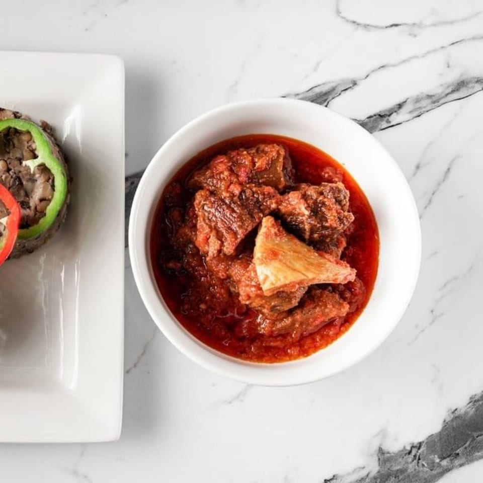 African stew with meat in a white bowl next to a plate with a molded dish.