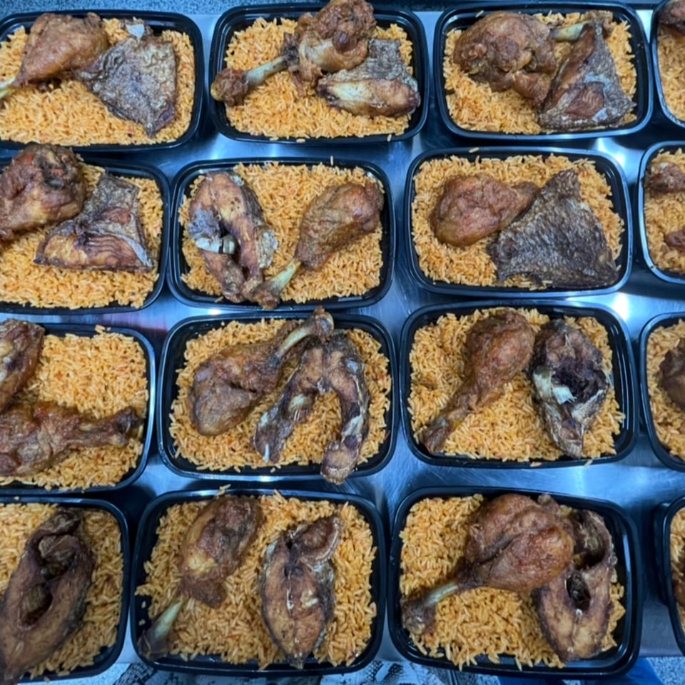 Multiple black containers filled with African jollof rice, fried chicken, and fish pieces.