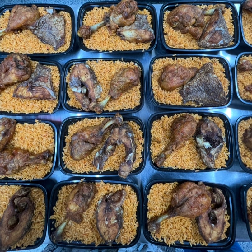 Multiple black containers filled with African jollof rice, fried chicken, and fish pieces.
