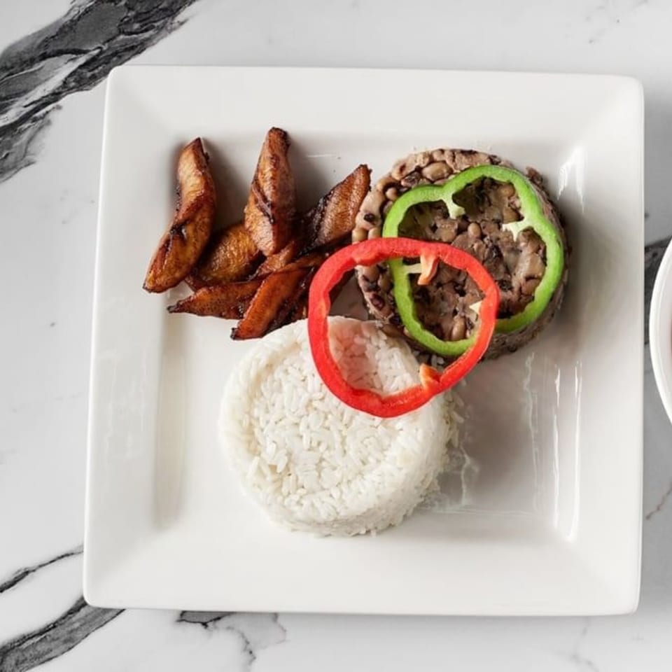 African meal with fried plantains, rice, beans, and bell pepper rings on a white plate.