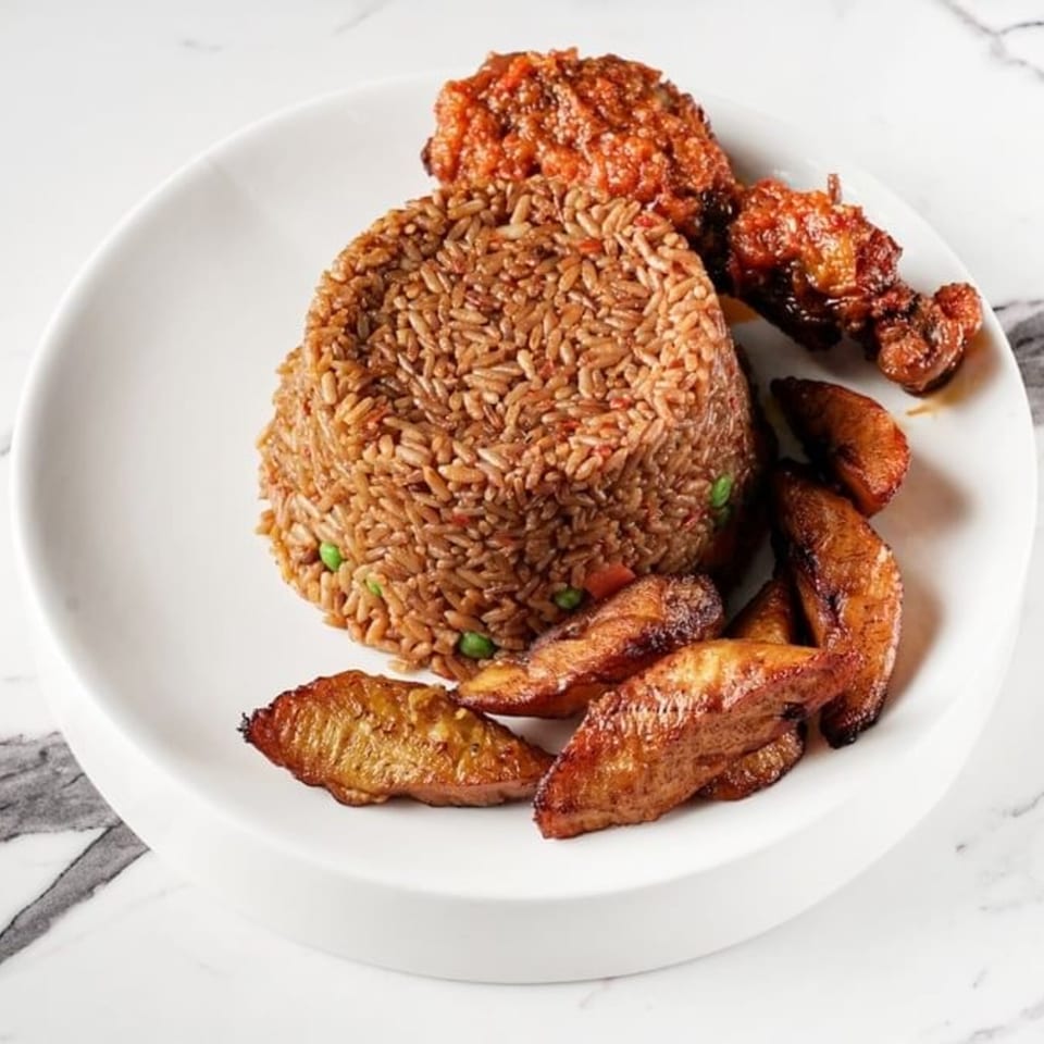 African Jollof rice with chicken and fried plantains on a white plate.