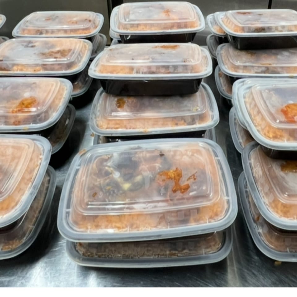 Numerous African cuisine takeout containers filled with food, stacked on a metal surface.