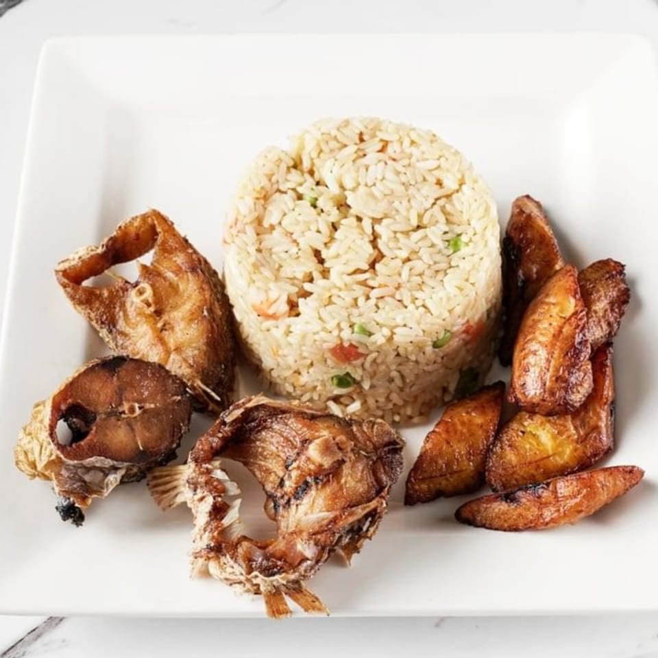 African fried rice with fried fish and plantains on a white rectangular plate.
