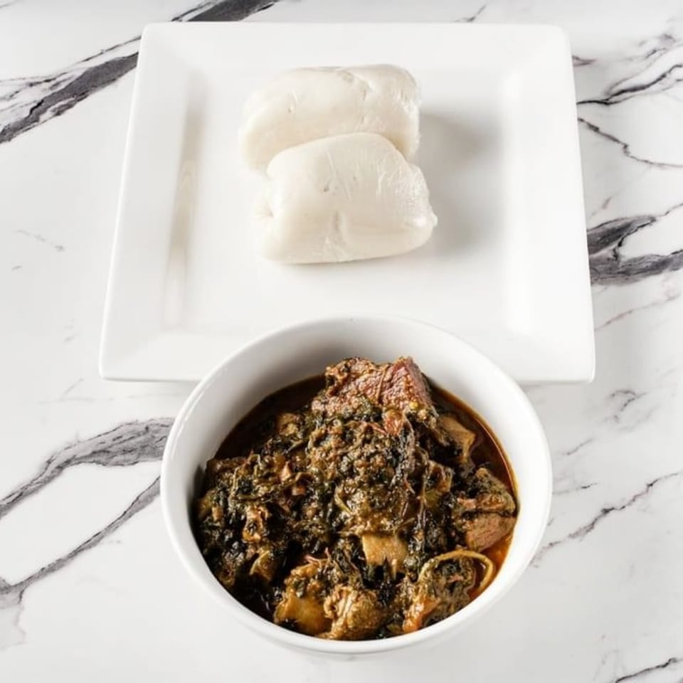 African dish with a bowl of dark stew and a plate of two white dough balls on marble.